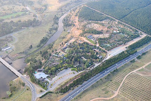 Aerial view of the National Zoo Aquarium - Canberra Guided Tours Aerial view of a river valley showing a multi-lane highway and bridge running past a wooded complex of buildings and parking lots, with surrounding forests, fields and a winding river.